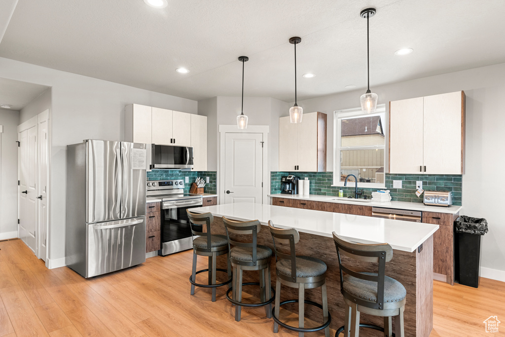 Kitchen featuring a kitchen island, light hardwood / wood-style flooring, appliances with stainless steel finishes, white cabinets, and hanging light fixtures