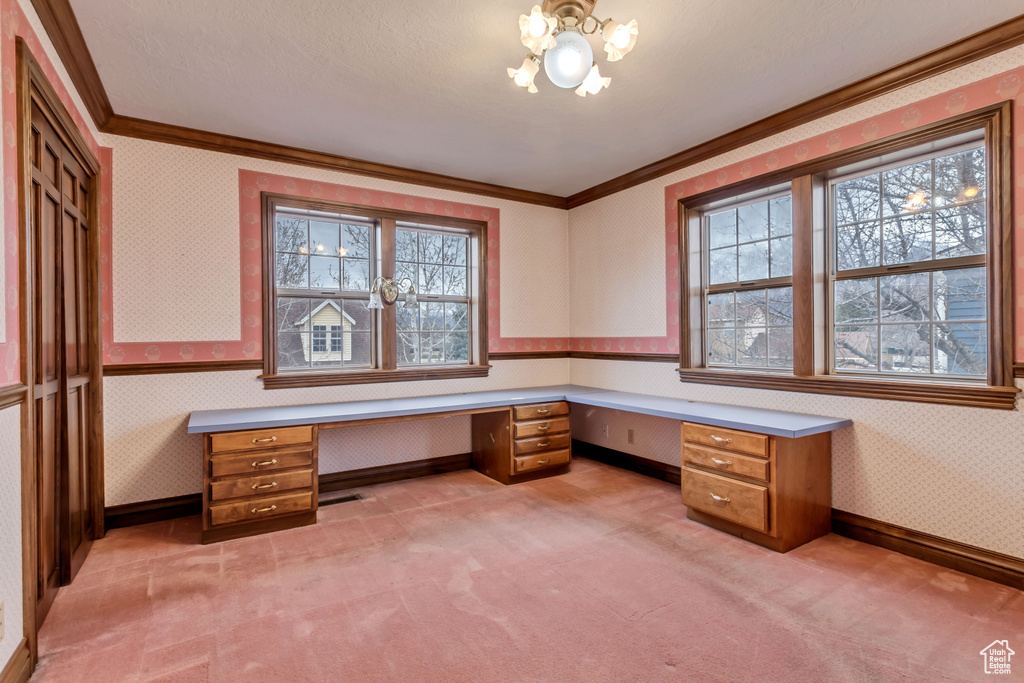 Unfurnished office with light colored carpet, crown molding, built in desk, and an inviting chandelier