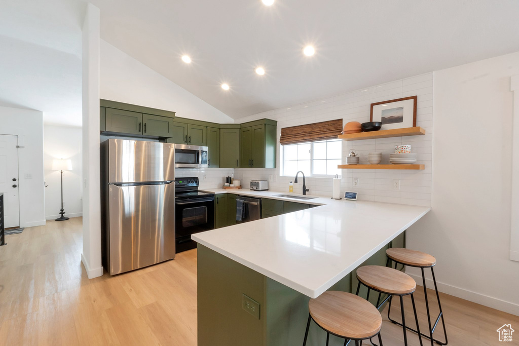 Kitchen featuring stainless steel appliances, light hardwood / wood-style floors, a kitchen bar, green cabinetry, and backsplash