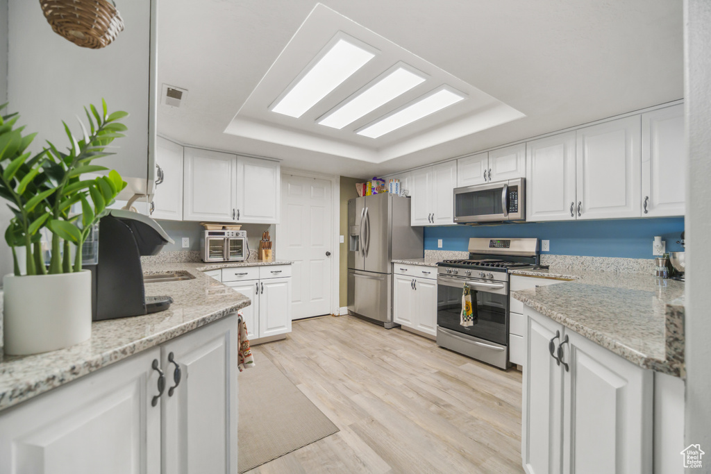 Kitchen featuring white cabinets, light stone countertops, stainless steel appliances, and light hardwood / wood-style flooring