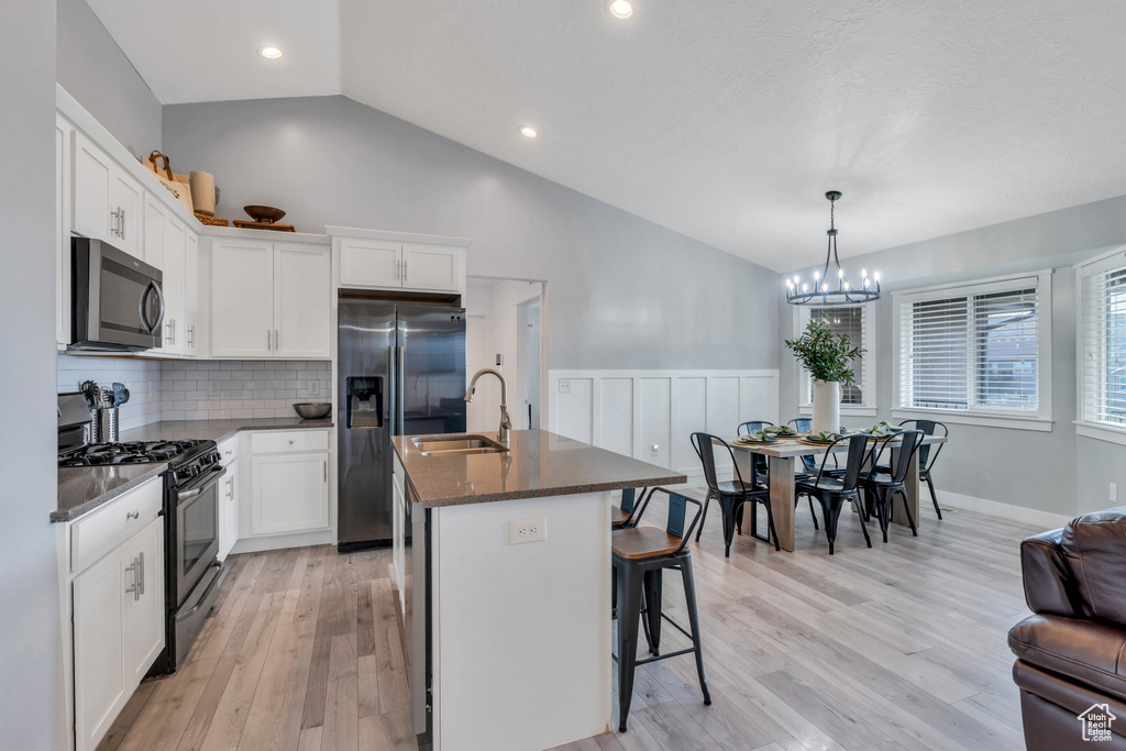 Kitchen featuring a kitchen island with sink, a chandelier, light hardwood / wood-style flooring, stainless steel appliances, and lofted ceiling