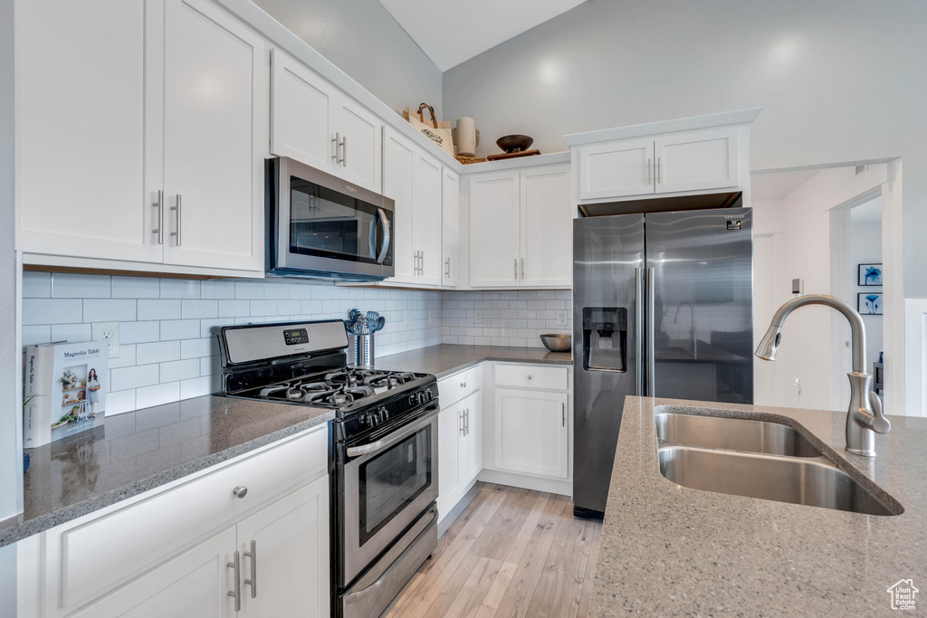 Kitchen with stainless steel appliances, light stone countertops, light hardwood / wood-style flooring, backsplash, and sink