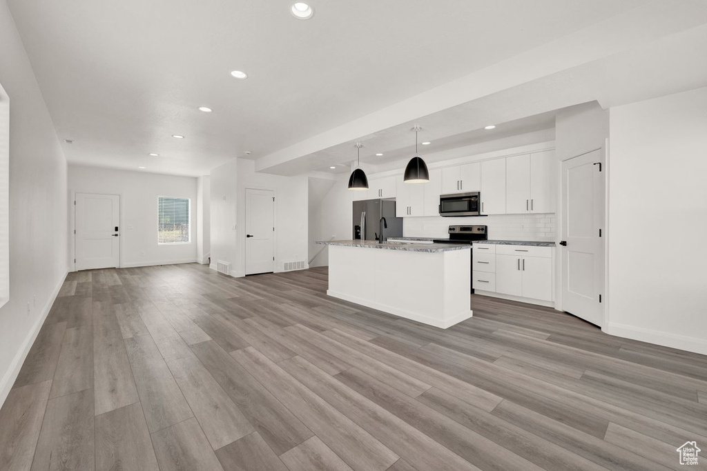 Kitchen with white cabinetry, light hardwood / wood-style flooring, stainless steel appliances, a center island with sink, and light stone counters