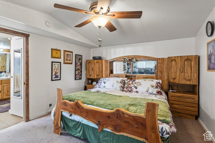 Bedroom with light colored carpet, vaulted ceiling, ensuite bath, and ceiling fan