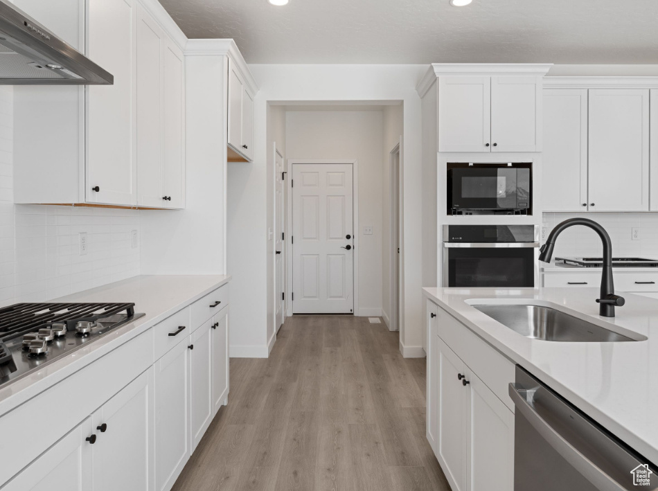 Kitchen with range hood, white cabinets, light hardwood / wood-style floors, stainless steel appliances, and tasteful backsplash