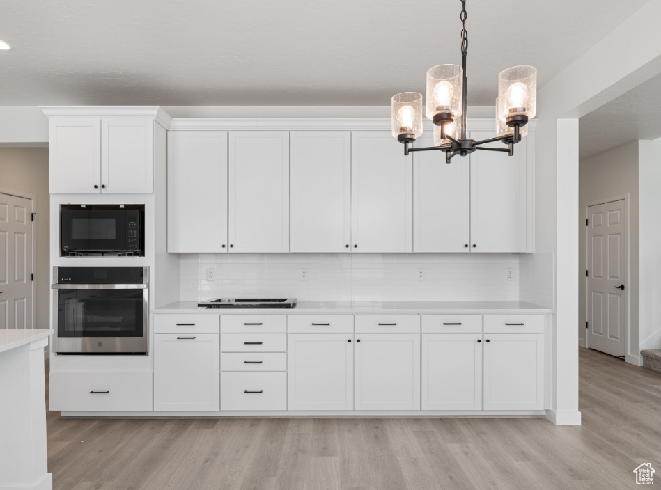 Kitchen featuring oven, black microwave, a notable chandelier, light hardwood / wood-style floors, and pendant lighting