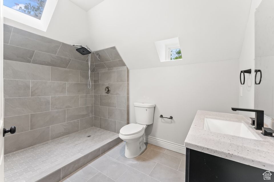 Bathroom featuring toilet, vanity, lofted ceiling with skylight, tile floors, and a tile shower