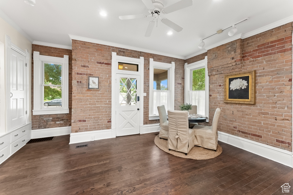 Unfurnished room featuring brick wall, ceiling fan, crown molding, rail lighting, and dark hardwood / wood-style flooring