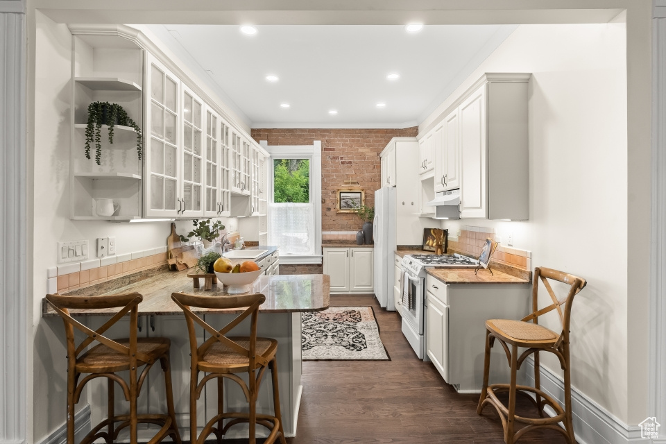 Kitchen with white appliances, white cabinetry, dark hardwood / wood-style floors, and premium range hood