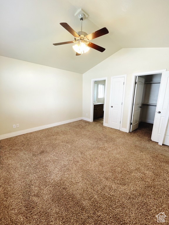 Unfurnished bedroom with ensuite bath, lofted ceiling, dark colored carpet, and ceiling fan