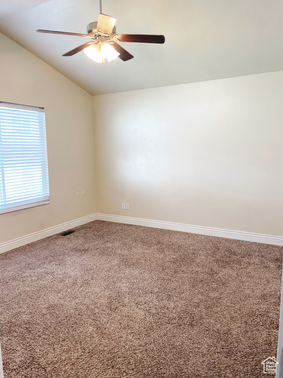 Empty room with ceiling fan, carpet floors, and vaulted ceiling
