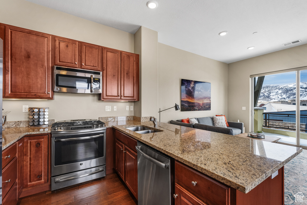 Kitchen with dark hardwood / wood-style floors, light stone countertops, stainless steel appliances, and kitchen peninsula