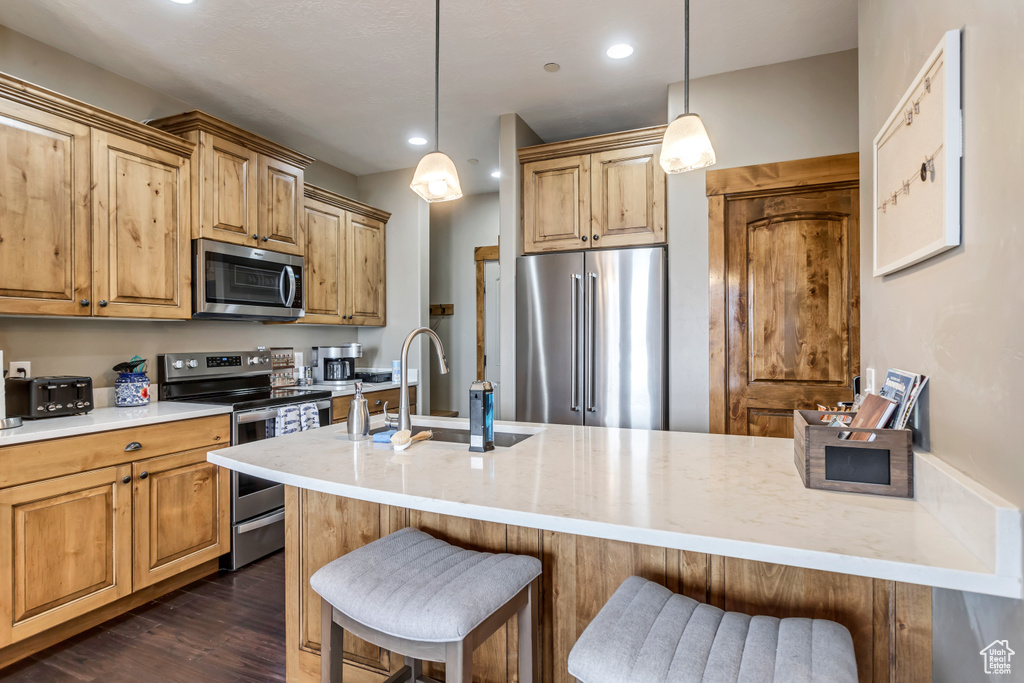 Kitchen with light stone countertops, appliances with stainless steel finishes, a breakfast bar, dark hardwood / wood-style flooring, and pendant lighting