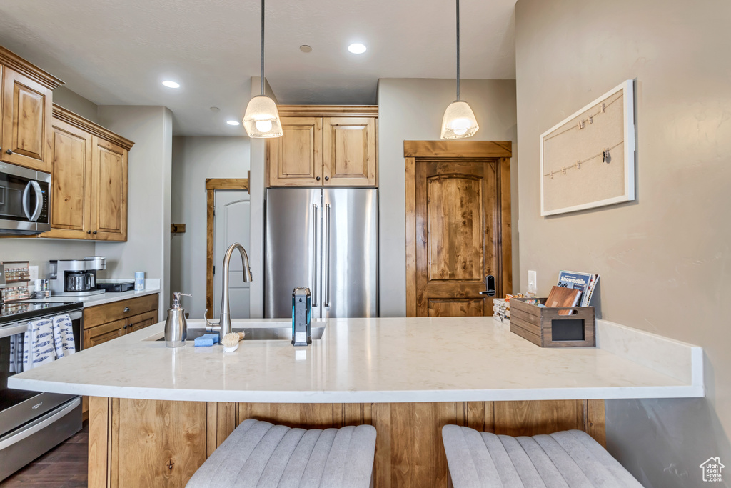 Kitchen featuring a kitchen breakfast bar, decorative light fixtures, appliances with stainless steel finishes, and dark wood-type flooring