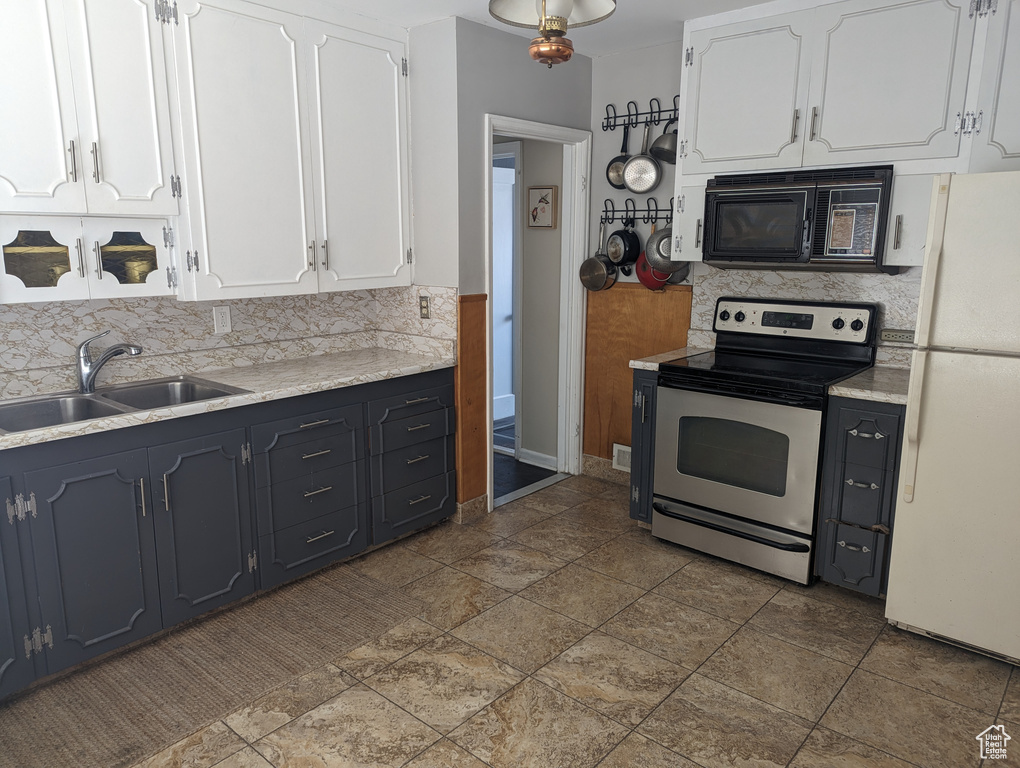 Kitchen with sink, white fridge, dark tile flooring, white cabinets, and stainless steel electric range oven