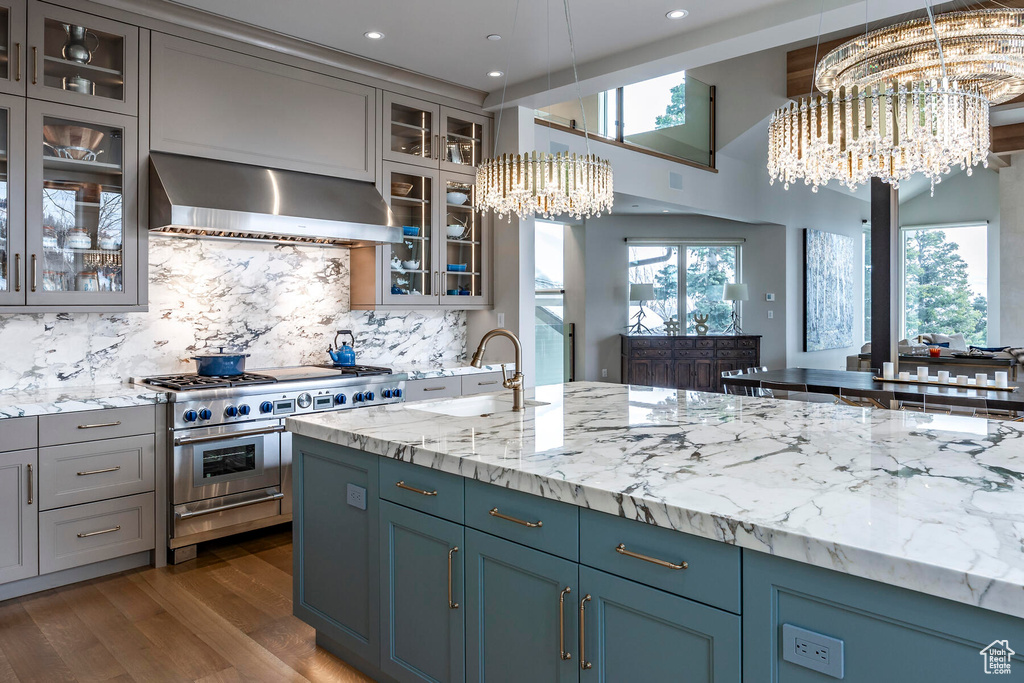 Kitchen with an inviting chandelier, wall chimney range hood, pendant lighting, and double oven range