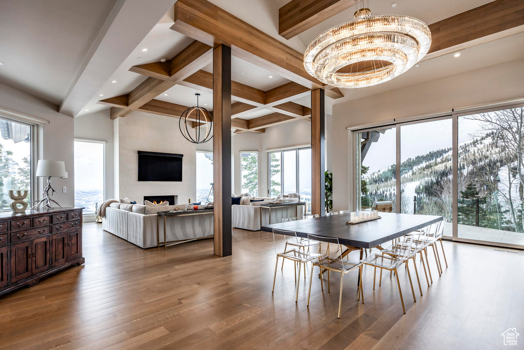 Dining space featuring wood-type flooring, beam ceiling, a fireplace, and an inviting chandelier