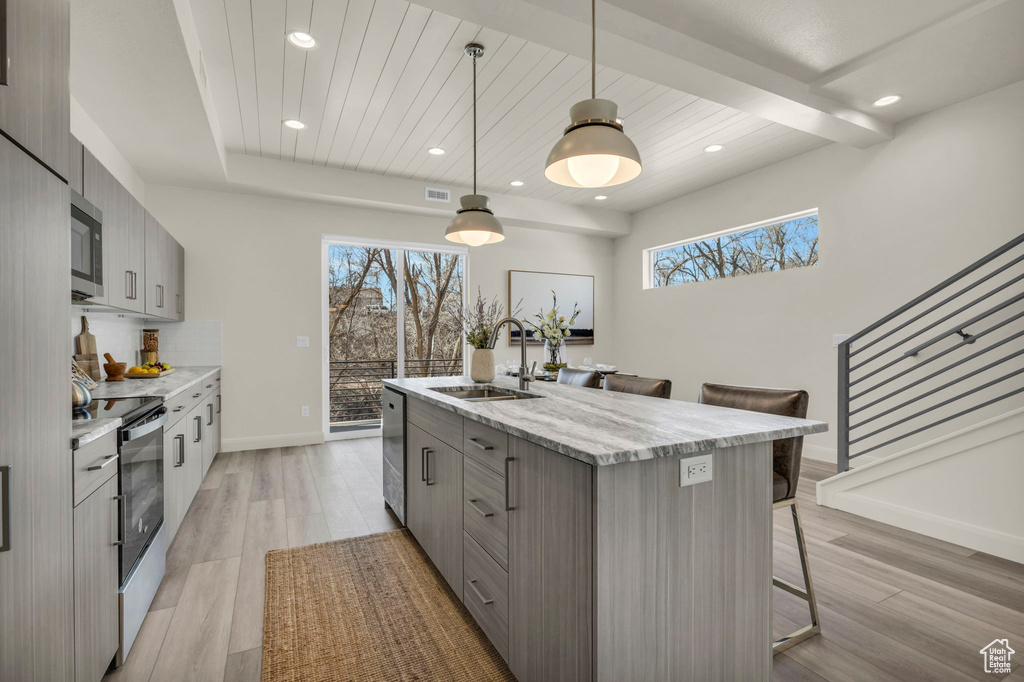 Kitchen with a breakfast bar area, a center island with sink, stainless steel appliances, light hardwood / wood-style floors, and decorative light fixtures