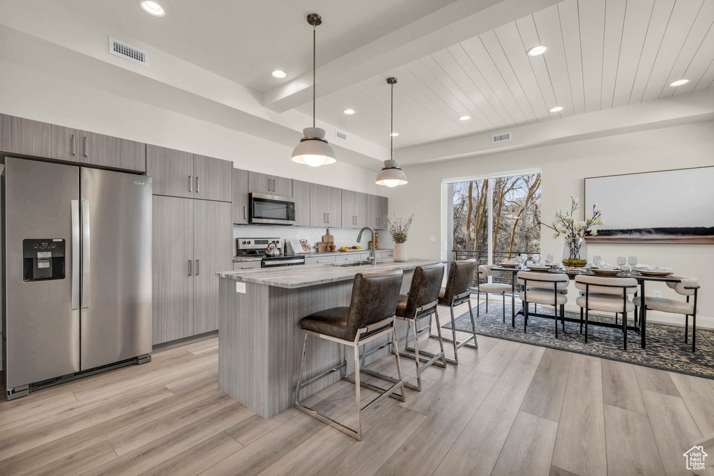 Kitchen featuring hanging light fixtures, appliances with stainless steel finishes, a breakfast bar, light wood-type flooring, and light stone counters