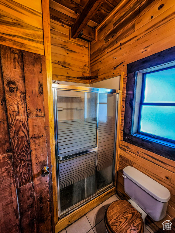 Bathroom featuring toilet, beam ceiling, wooden walls, tile floors, and an enclosed shower