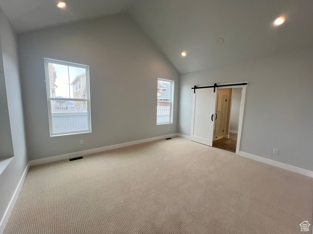 Unfurnished bedroom with a barn door, light carpet, and high vaulted ceiling