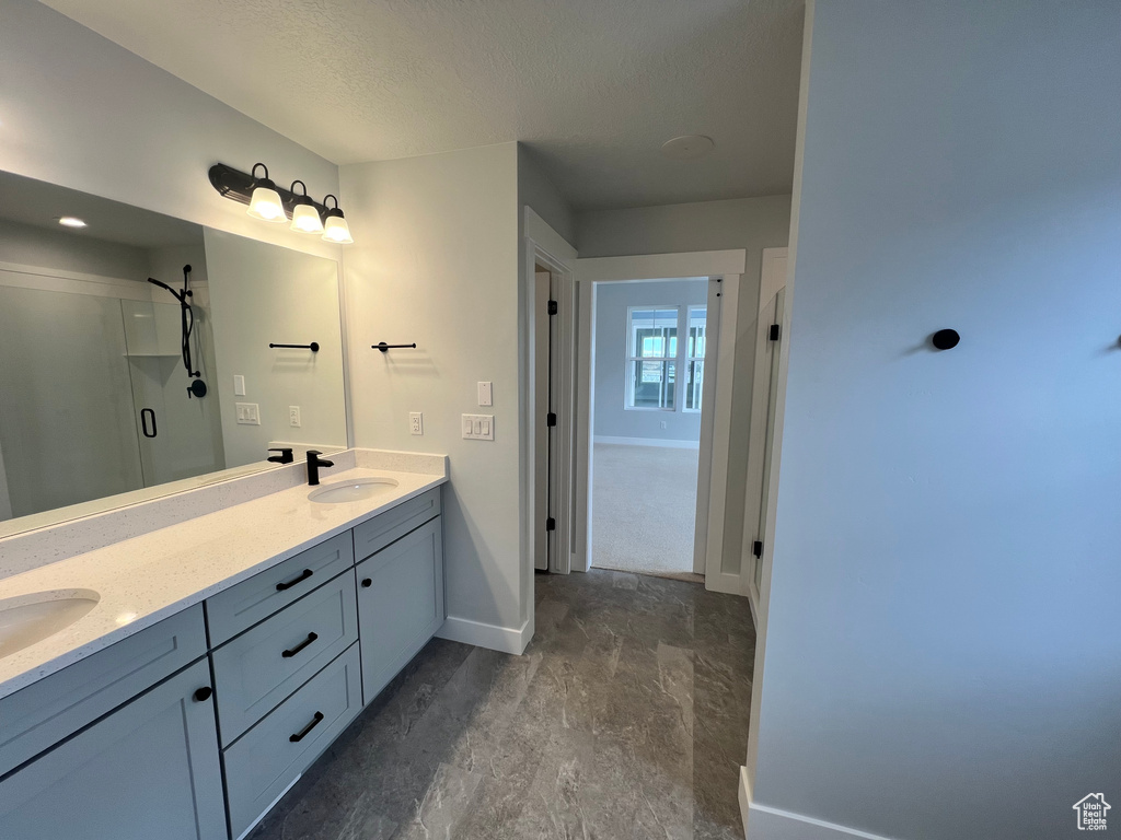 Bathroom featuring double sink vanity, tile flooring, walk in shower, and a textured ceiling