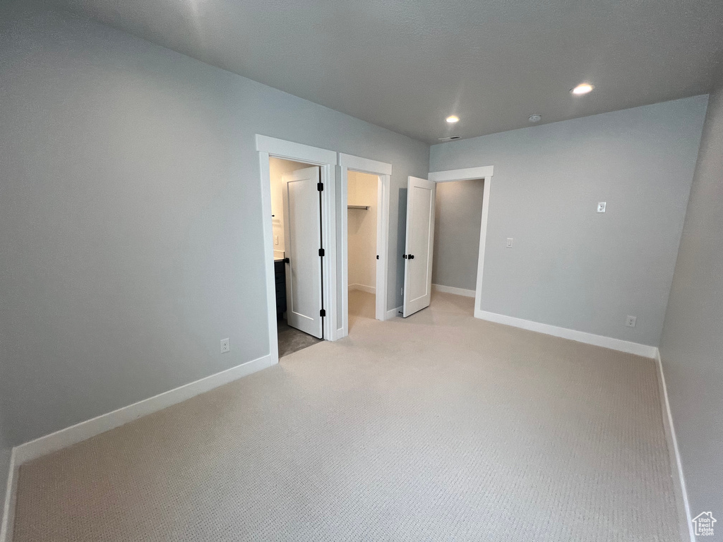 Unfurnished bedroom with light carpet, a spacious closet, and a closet