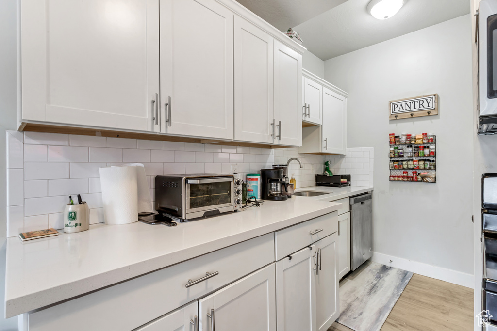 Kitchen featuring stainless steel dishwasher, tasteful backsplash, light hardwood / wood-style flooring, white cabinets, and sink