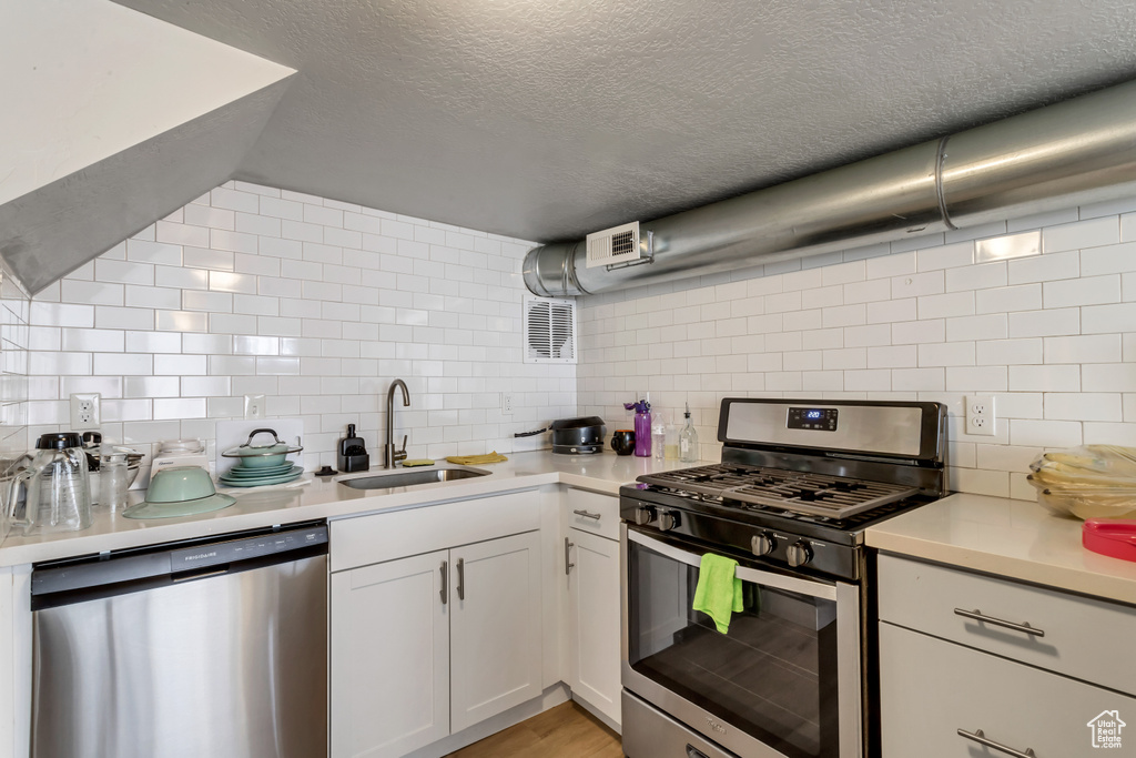 Kitchen featuring stainless steel appliances, a textured ceiling, white cabinetry, backsplash, and sink