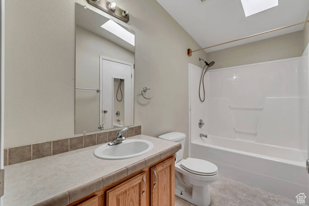 Full bathroom with toilet, shower / bathing tub combination, vaulted ceiling with skylight, vanity, and tile floors