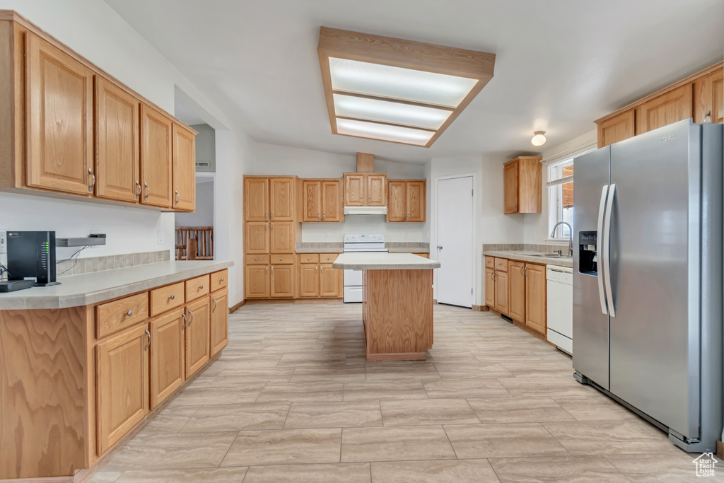 Kitchen featuring white appliances, a center island, sink, and light tile floors