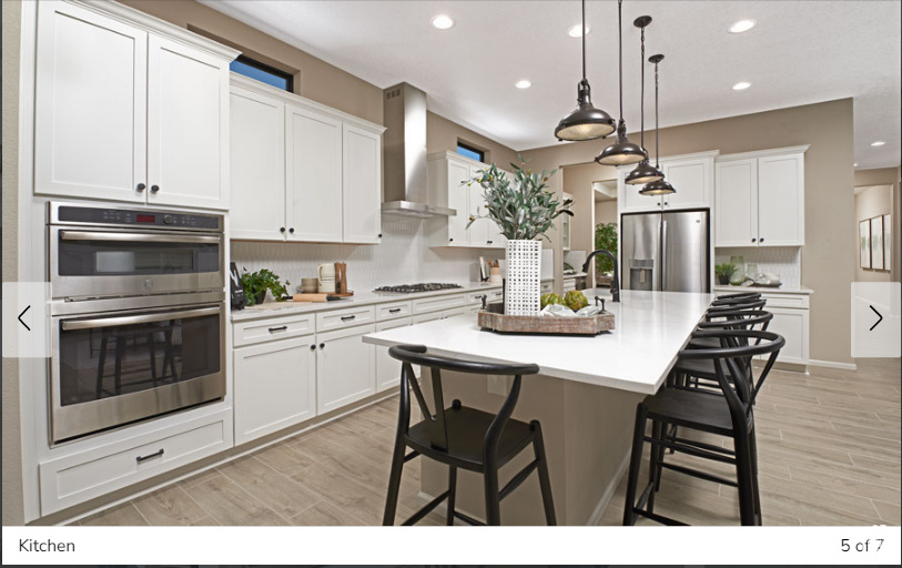 Kitchen featuring stainless steel appliances, wall chimney exhaust hood, white cabinetry, backsplash, and hanging light fixtures