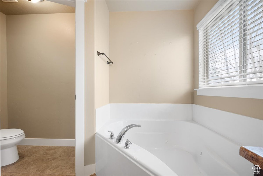 Bathroom with toilet, tile floors, a bathtub, and a wealth of natural light