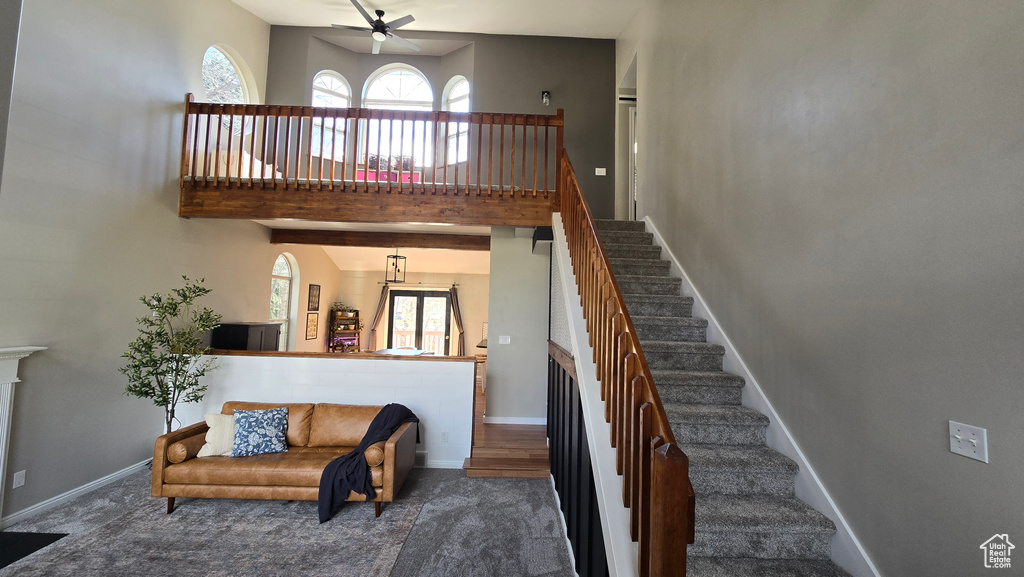 Stairway with plenty of natural light, ceiling fan with notable chandelier, dark carpet, and a high ceiling