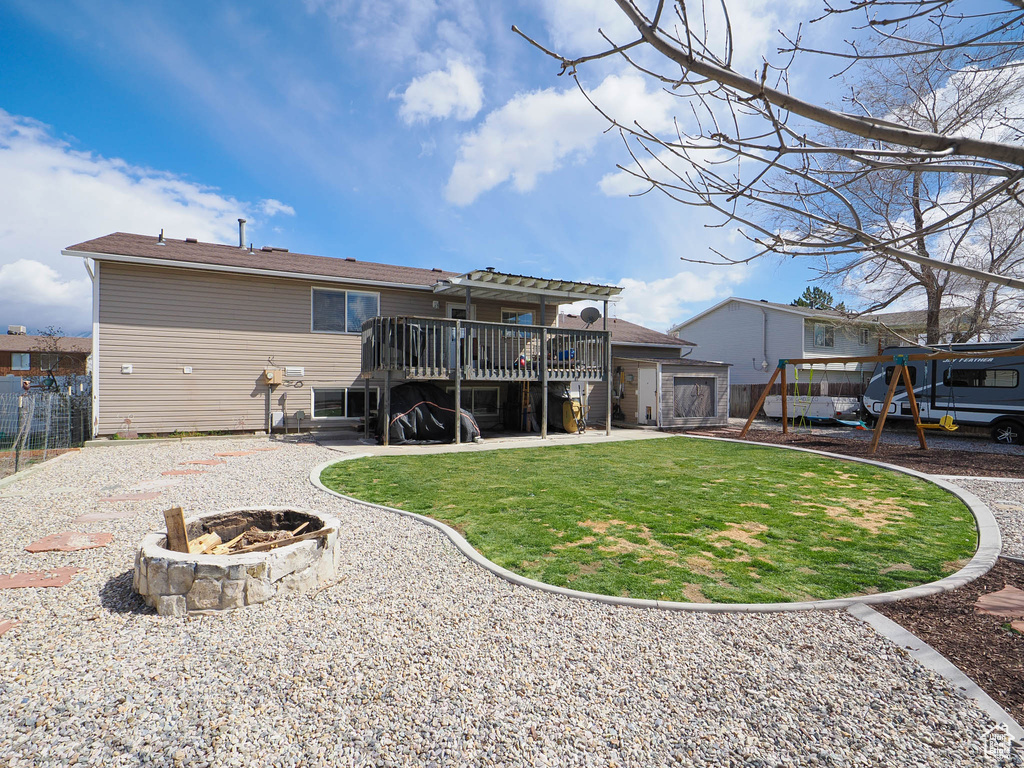 Rear view of property featuring a wooden deck, a lawn, a playground, an outdoor fire pit, and a patio area