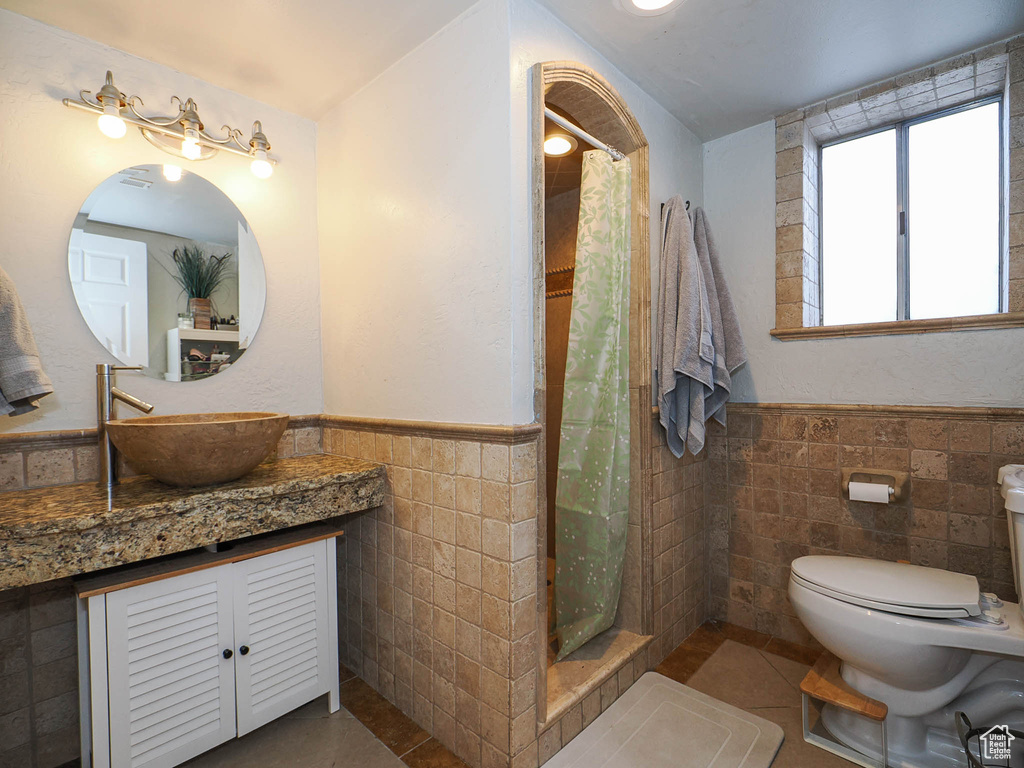 Bathroom featuring tile walls, toilet, vanity, and tile flooring
