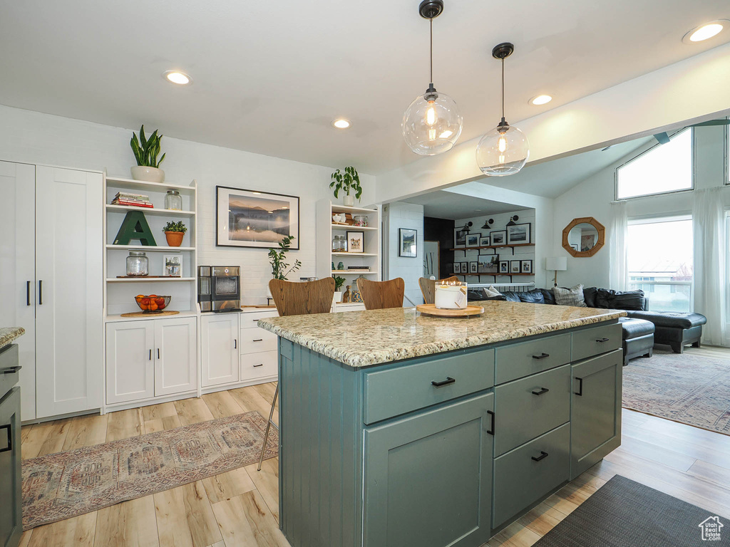 Kitchen with pendant lighting, a center island, light stone countertops, vaulted ceiling, and light hardwood / wood-style flooring