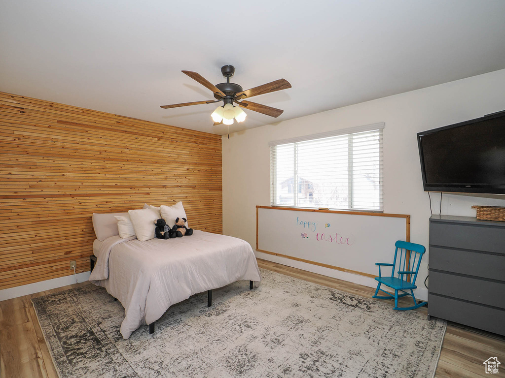 Bedroom with wooden walls, ceiling fan, and light wood-type flooring