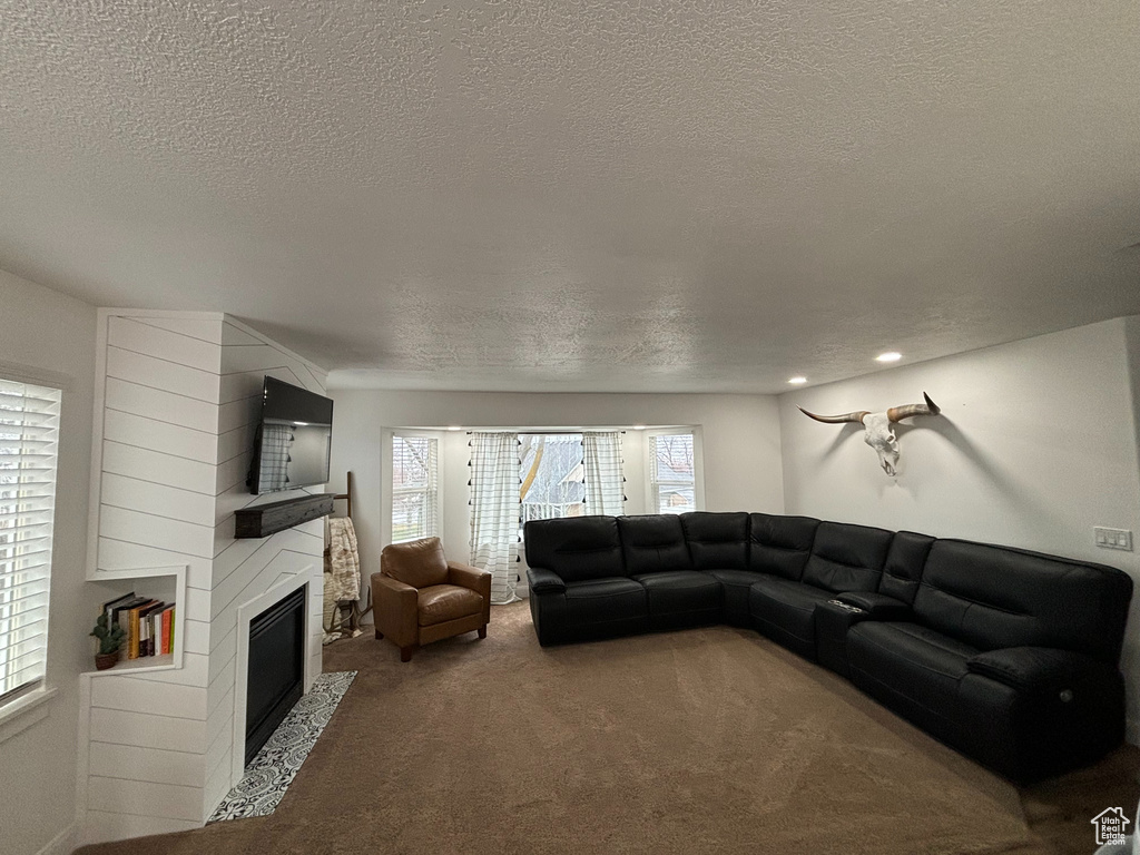 Living room with a textured ceiling, dark carpet, and a fireplace