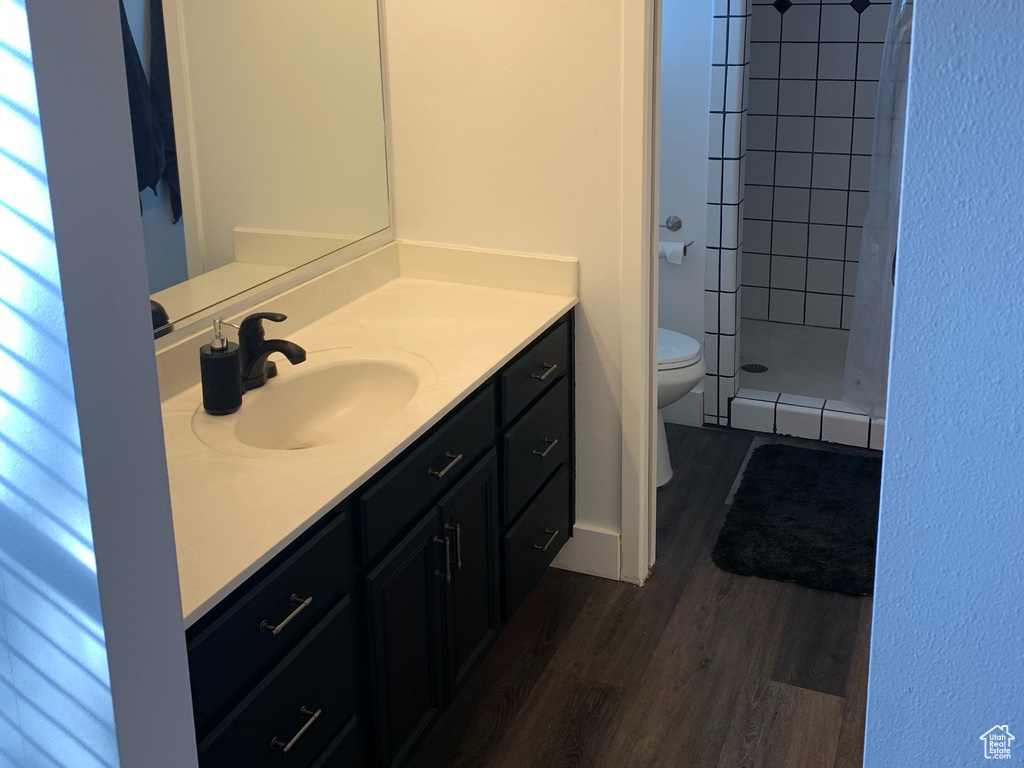Bathroom featuring vanity, hardwood / wood-style floors, a tile shower, and toilet