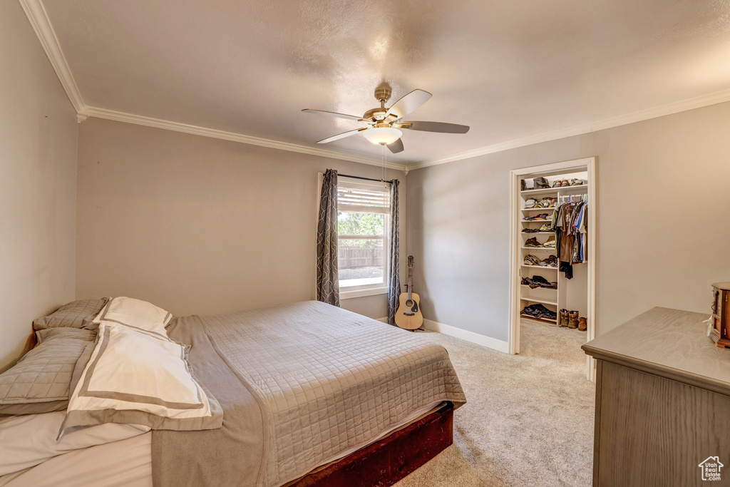 Carpeted bedroom featuring a closet, a spacious closet, crown molding, and ceiling fan
