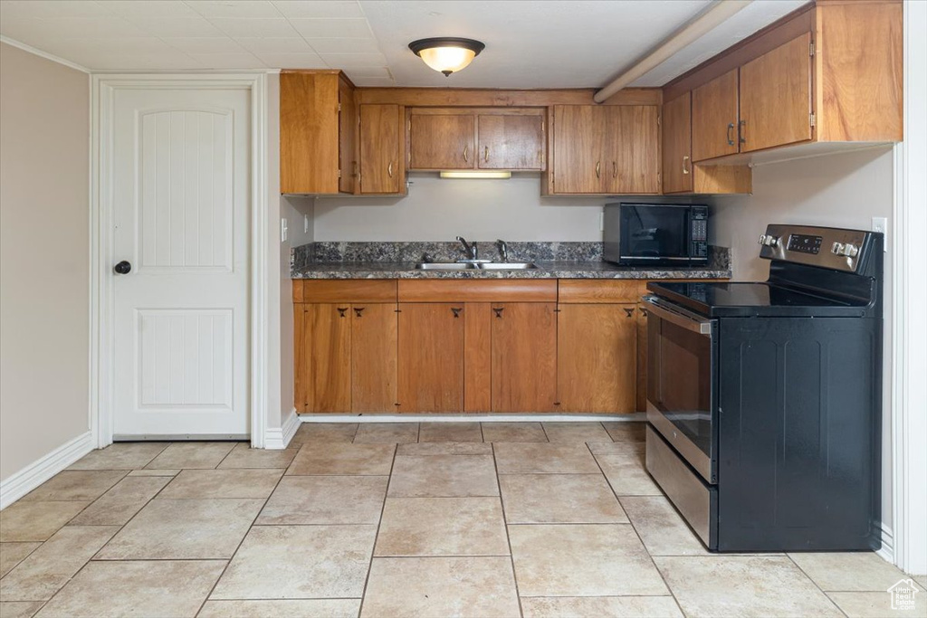 Kitchen with light tile floors, stainless steel electric range, dark stone countertops, and sink