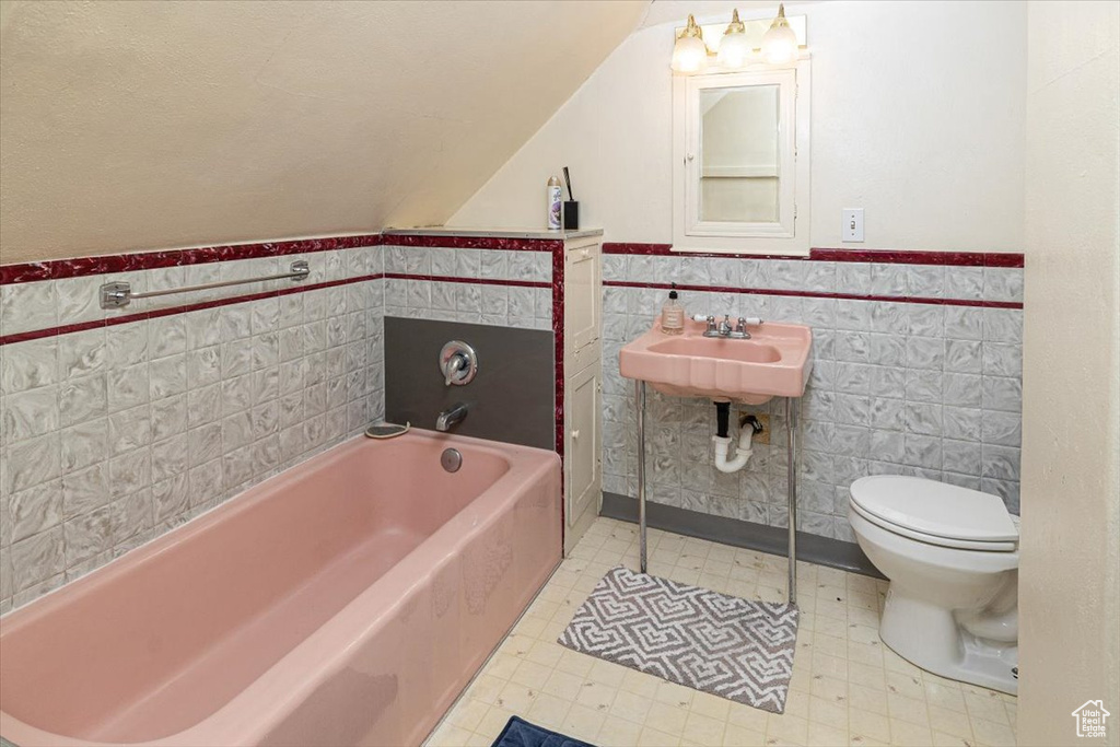 Bathroom featuring tile walls, toilet, sink, a bath to relax in, and tile flooring