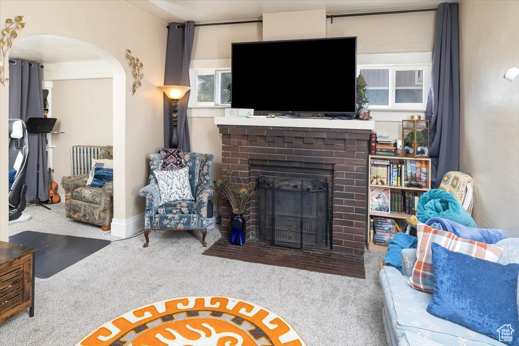 Carpeted living room featuring a fireplace and radiator heating unit