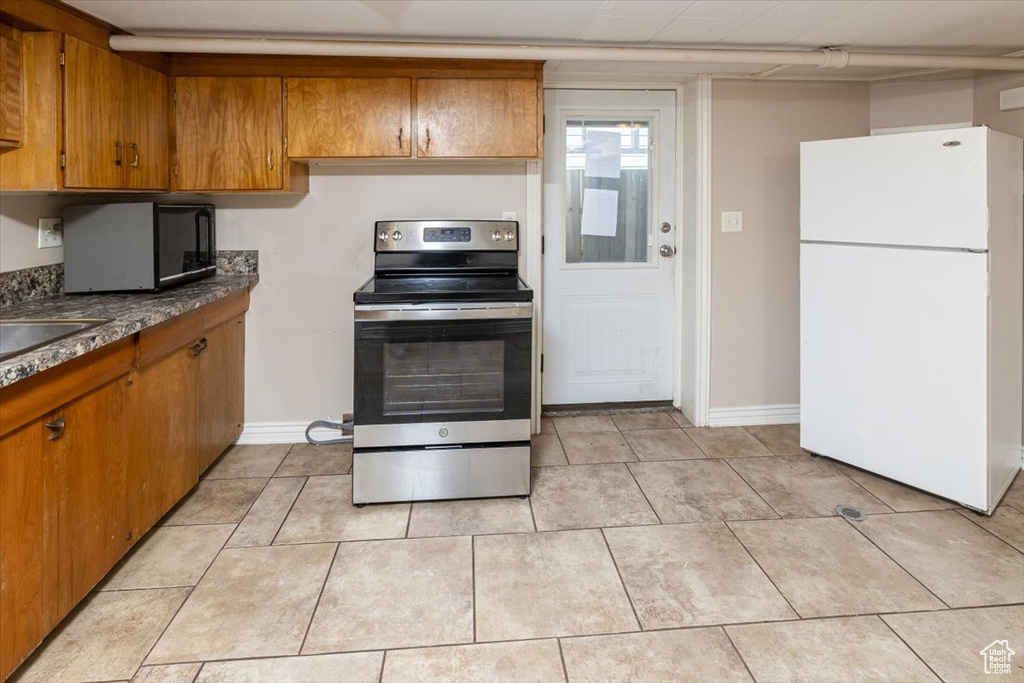 Kitchen with white refrigerator, stainless steel electric range oven, and light tile floors