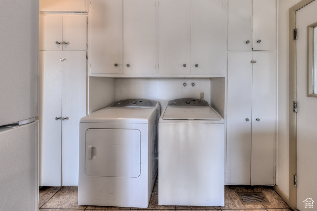 Clothes washing area featuring independent washer and dryer, light tile floors, and cabinets