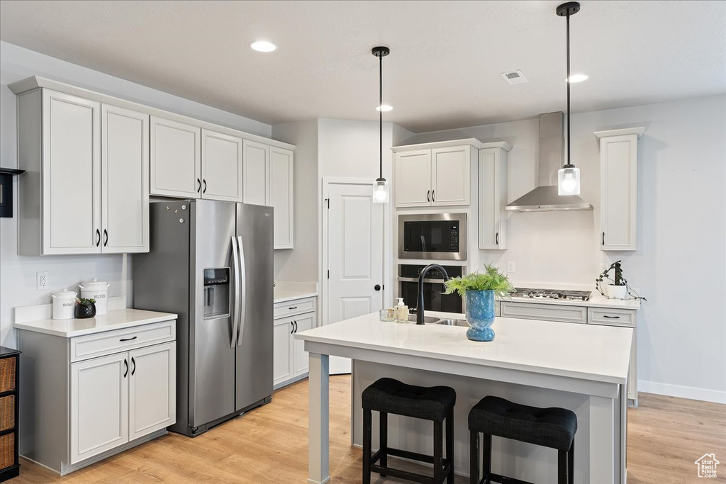 Kitchen featuring wall chimney range hood, light hardwood / wood-style floors, stainless steel appliances, and pendant lighting