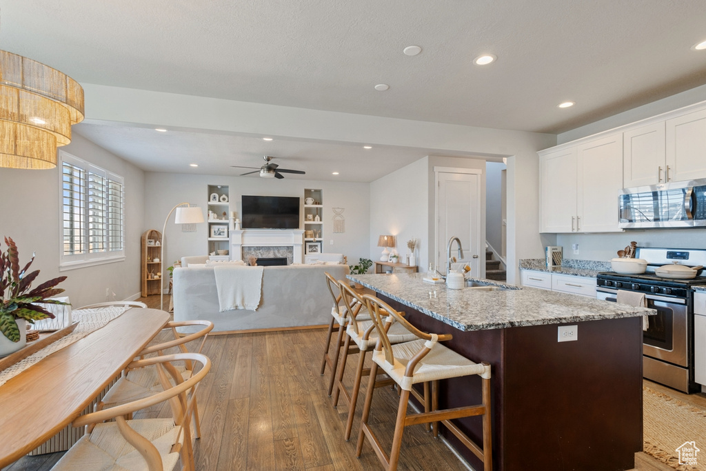 Kitchen featuring light hardwood / wood-style floors, stainless steel appliances, light stone countertops, white cabinetry, and sink