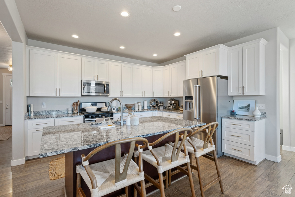 Kitchen with light stone countertops, light hardwood / wood-style floors, appliances with stainless steel finishes, and white cabinetry