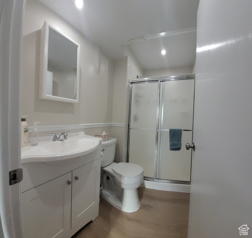 Bathroom with toilet, wood-type flooring, a shower with shower door, and vanity